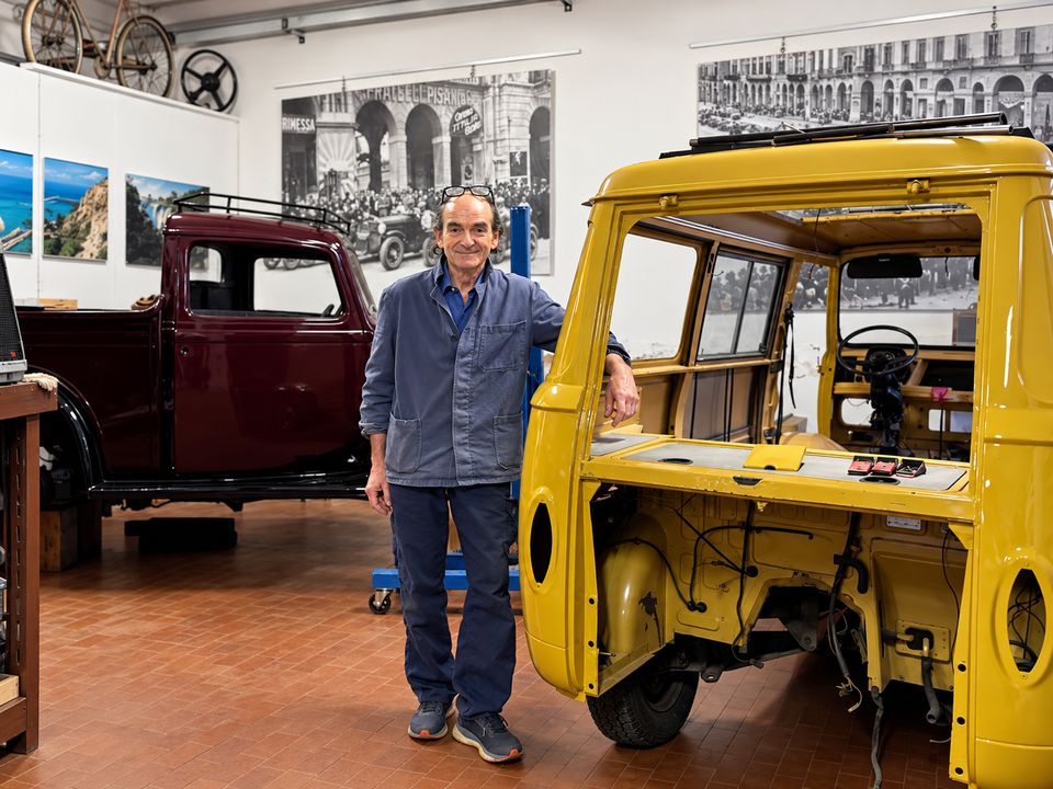 Mimmo Bongioanni in the workshop between a red car and a yellow van
